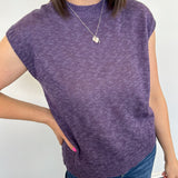 Person wearing a purple sleeveless sweater and blue jeans against a white background