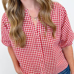 Woman wearing a red and white checkered shirt with blue jeans against a plain background