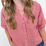 Woman wearing a red and white checkered shirt with blue jeans against a plain background