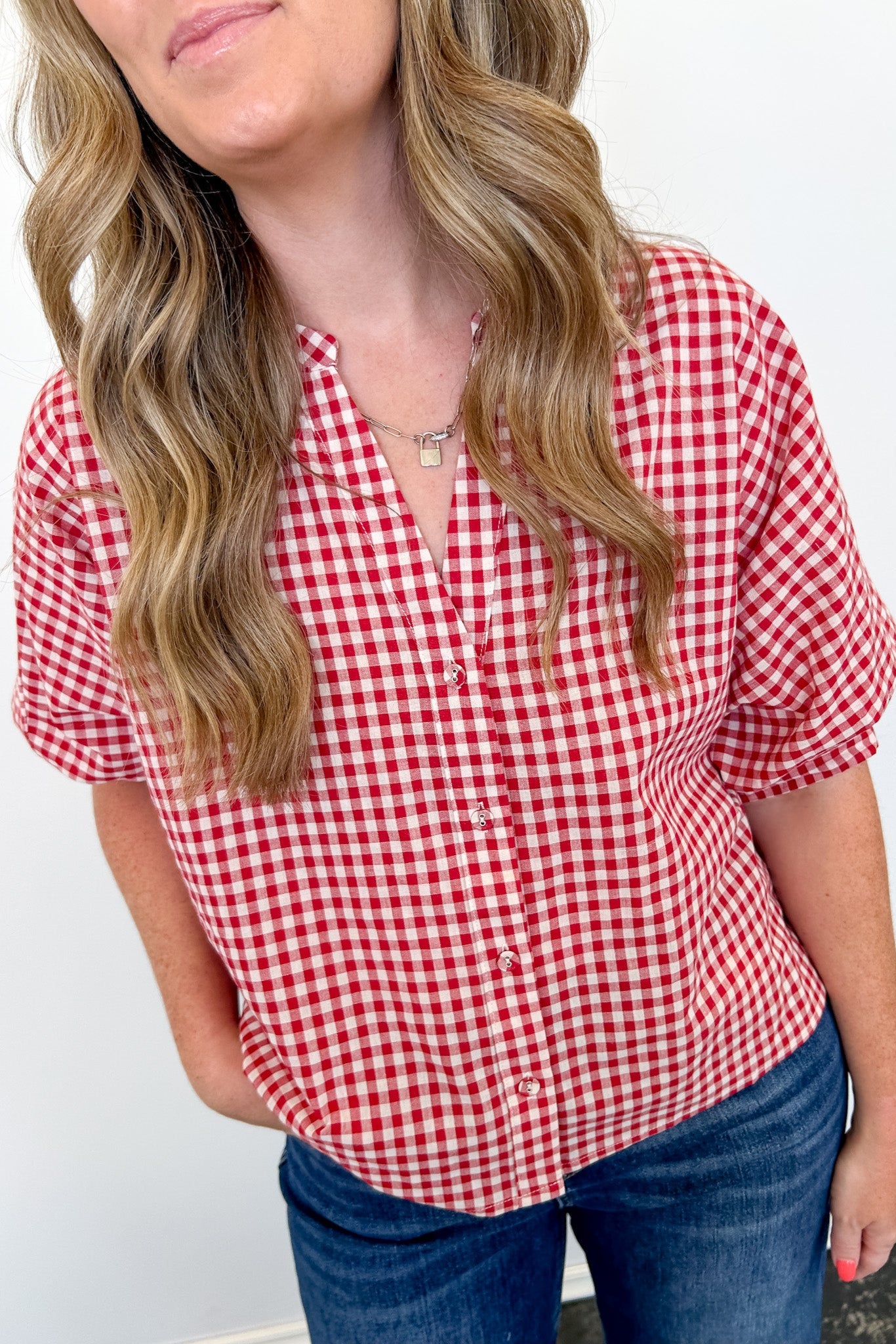 Woman wearing a red and white checkered shirt with blue jeans against a plain background