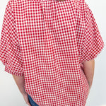 Person wearing a red and white checkered shirt with blue jeans against a white wall.
