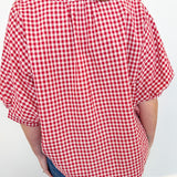 Person wearing a red and white checkered shirt with blue jeans against a white wall.
