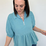 Woman wearing a light blue blouse with ruffled details against a white background