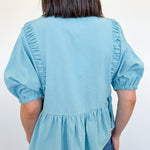 Light blue blouse with ruffled sleeves and bottom worn by a person against a white background