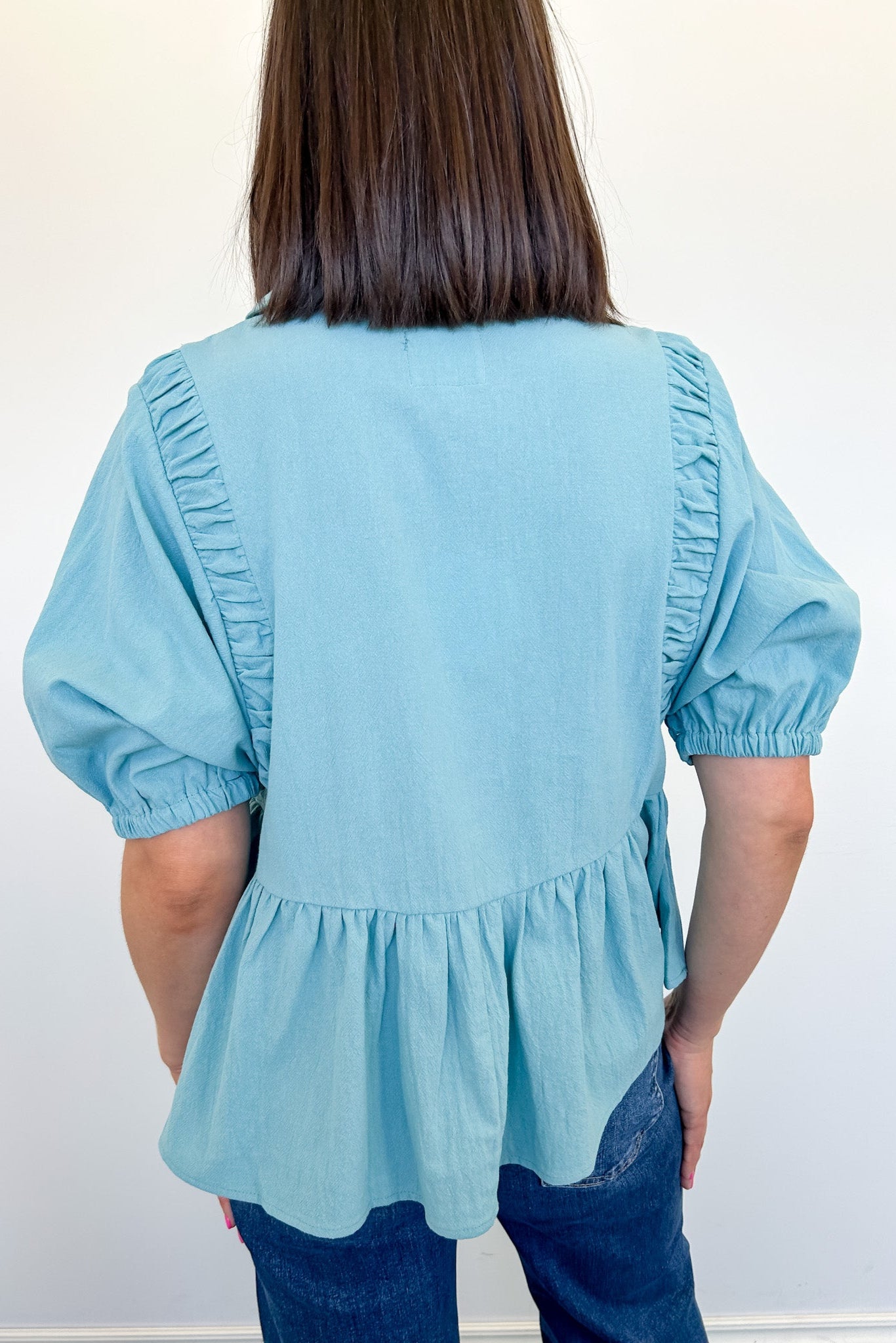 Light blue blouse with ruffled sleeves and bottom worn by a person against a white background