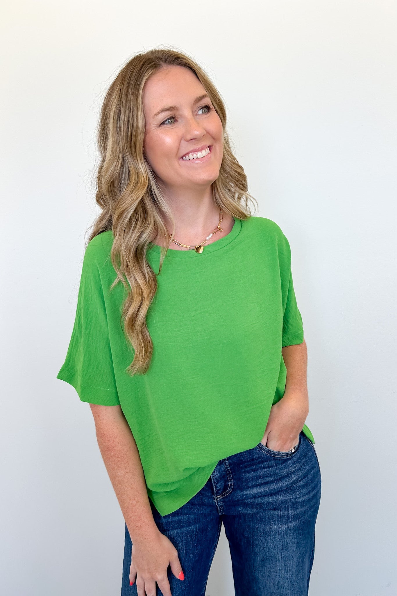 Woman wearing a green top and blue jeans against a white background