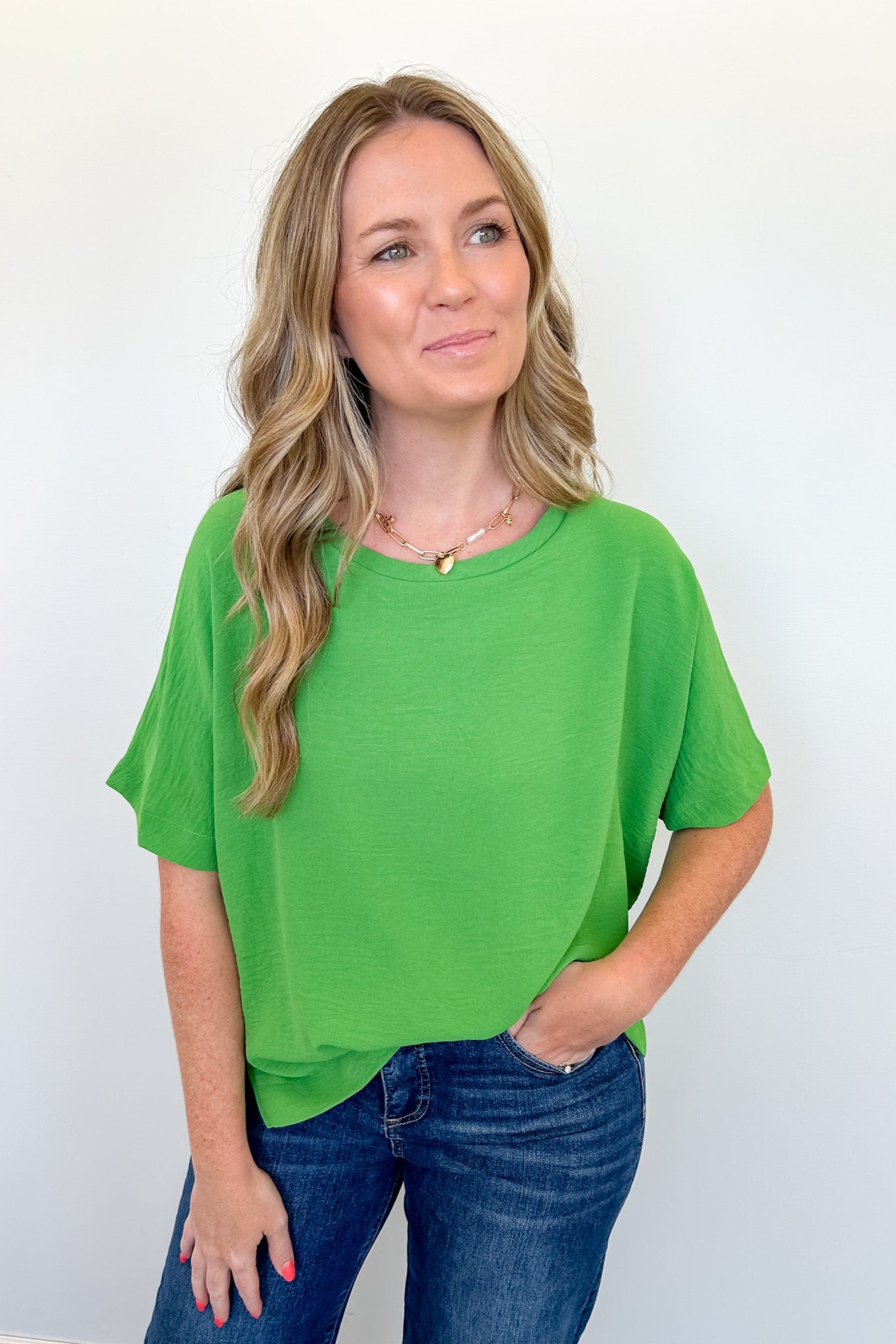 Woman wearing a green top and blue jeans against a white background