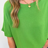 Person wearing a green top and blue jeans with a gold necklace against a white background