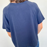 Person wearing a blue t-shirt and jeans against a white wall