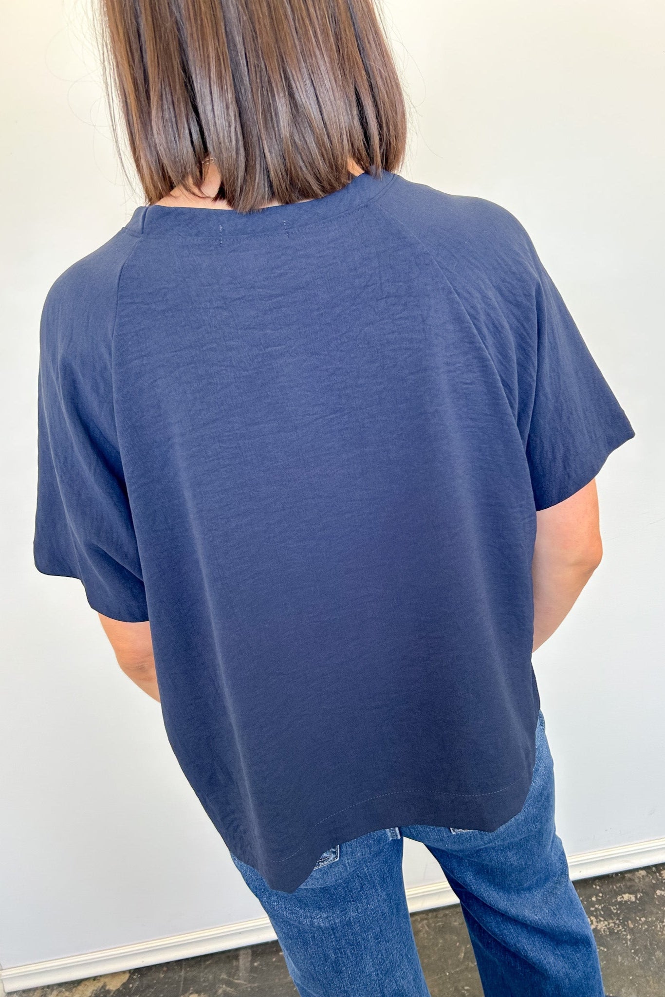 Person wearing a blue t-shirt and jeans against a white wall