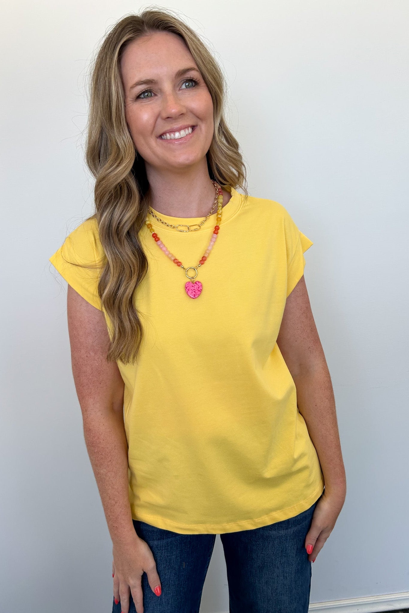Woman wearing a yellow top and blue jeans against a white background