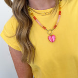 Person wearing a yellow shirt and colorful beaded necklace with a pink heart pendant on a white background