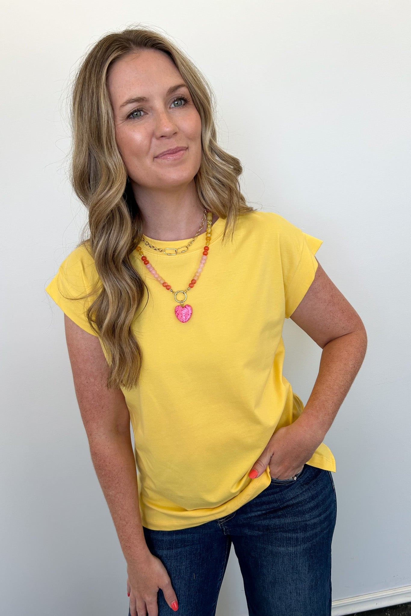 Woman wearing a yellow top and blue jeans against a white background