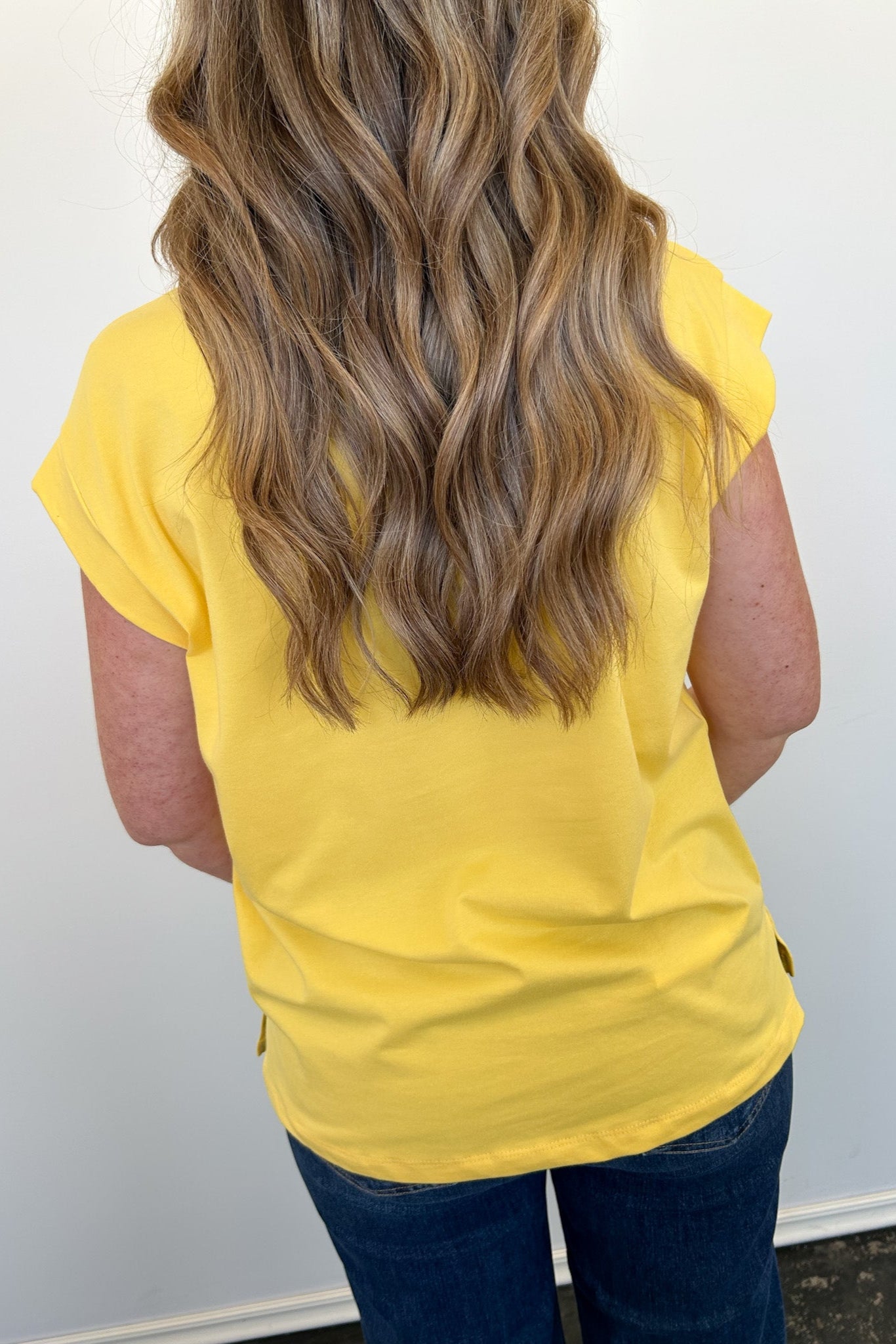 Person wearing a yellow sleeveless top with a plain background