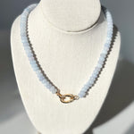 Necklace with light blue beads on a white bust against a gray background