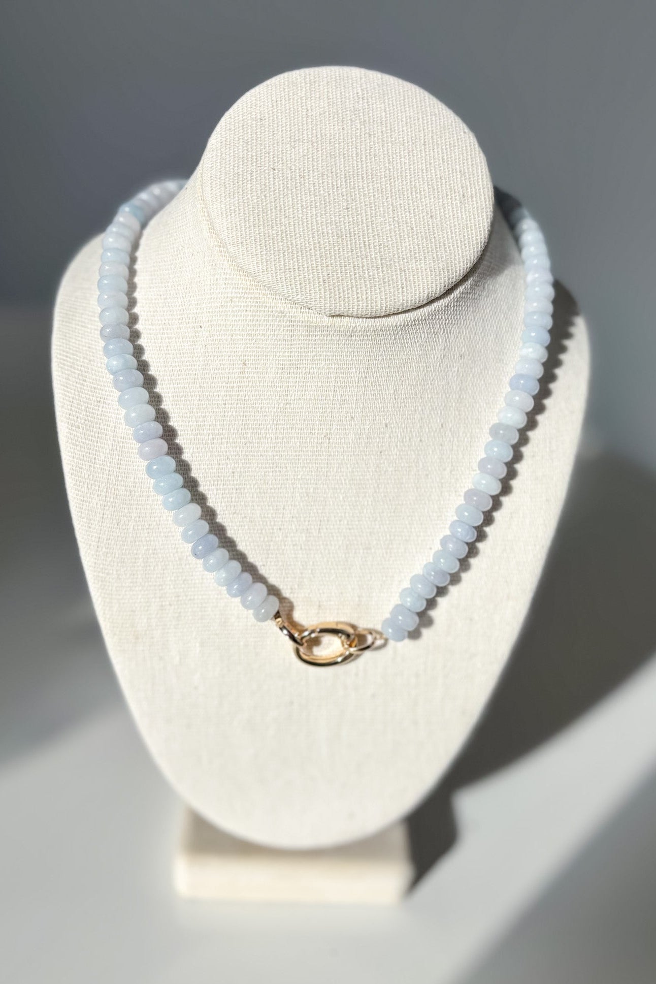 Necklace with light blue beads on a white bust against a gray background