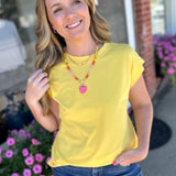 Woman in a yellow shirt standing outdoors with flowers and a building in the background