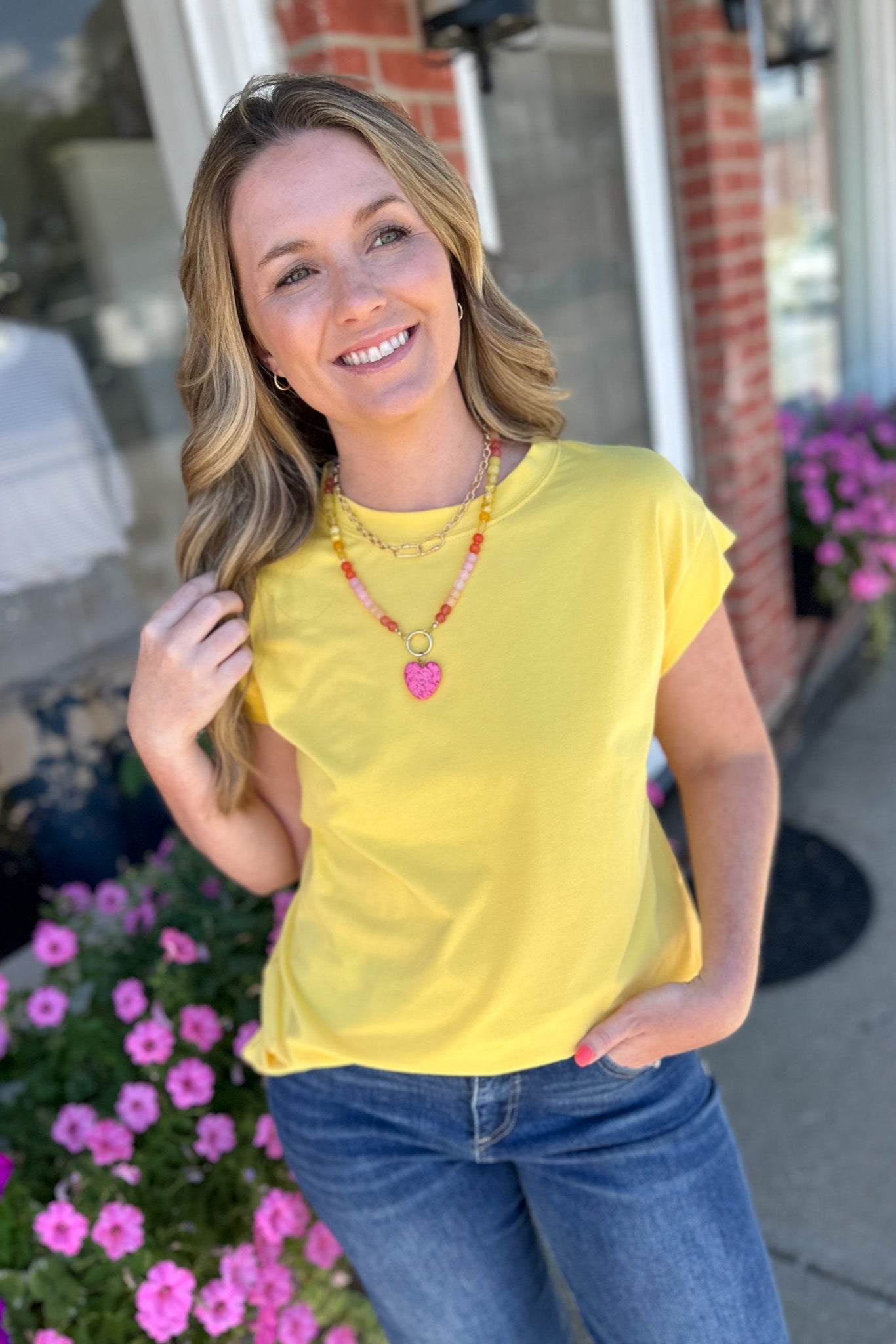 Woman in a yellow shirt standing outdoors with flowers and a building in the background