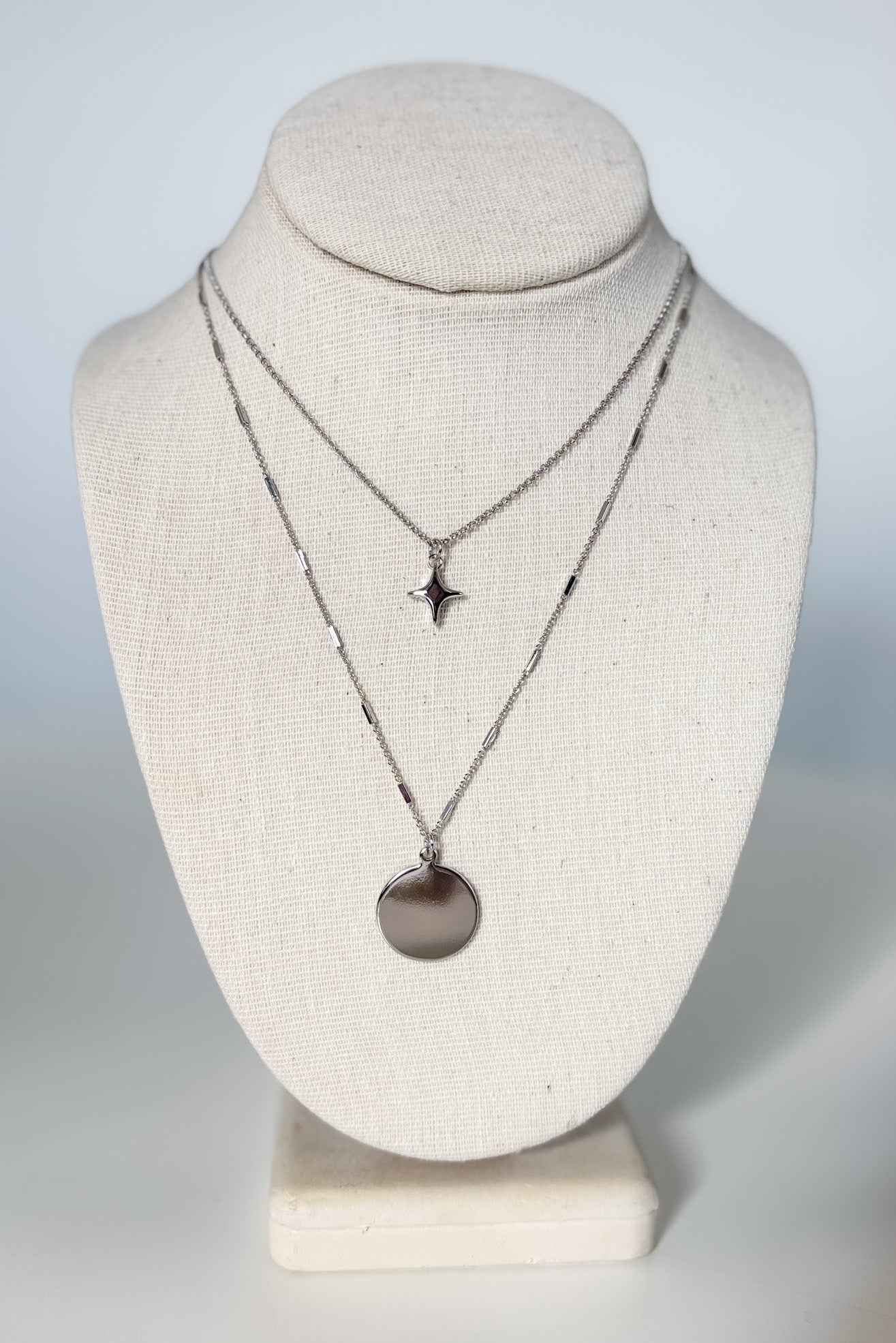 Two necklaces on a mannequin bust against a plain background