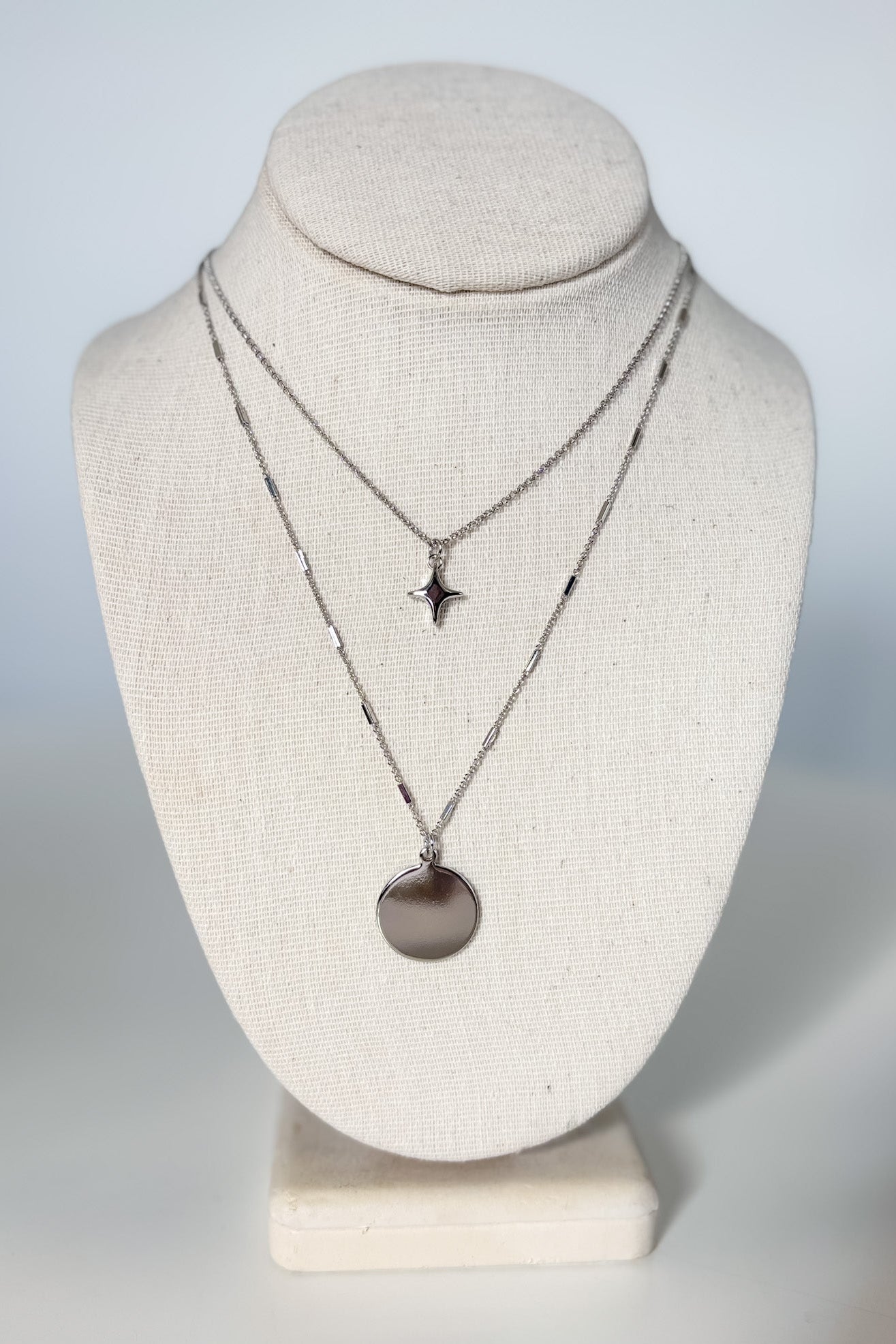 Two necklaces on a mannequin bust against a plain background