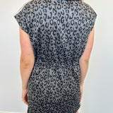 Person wearing a black and gray leopard print dress against a white wall.