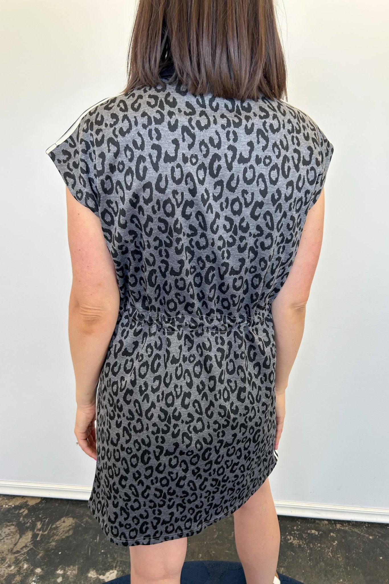 Person wearing a black and gray leopard print dress against a white wall.