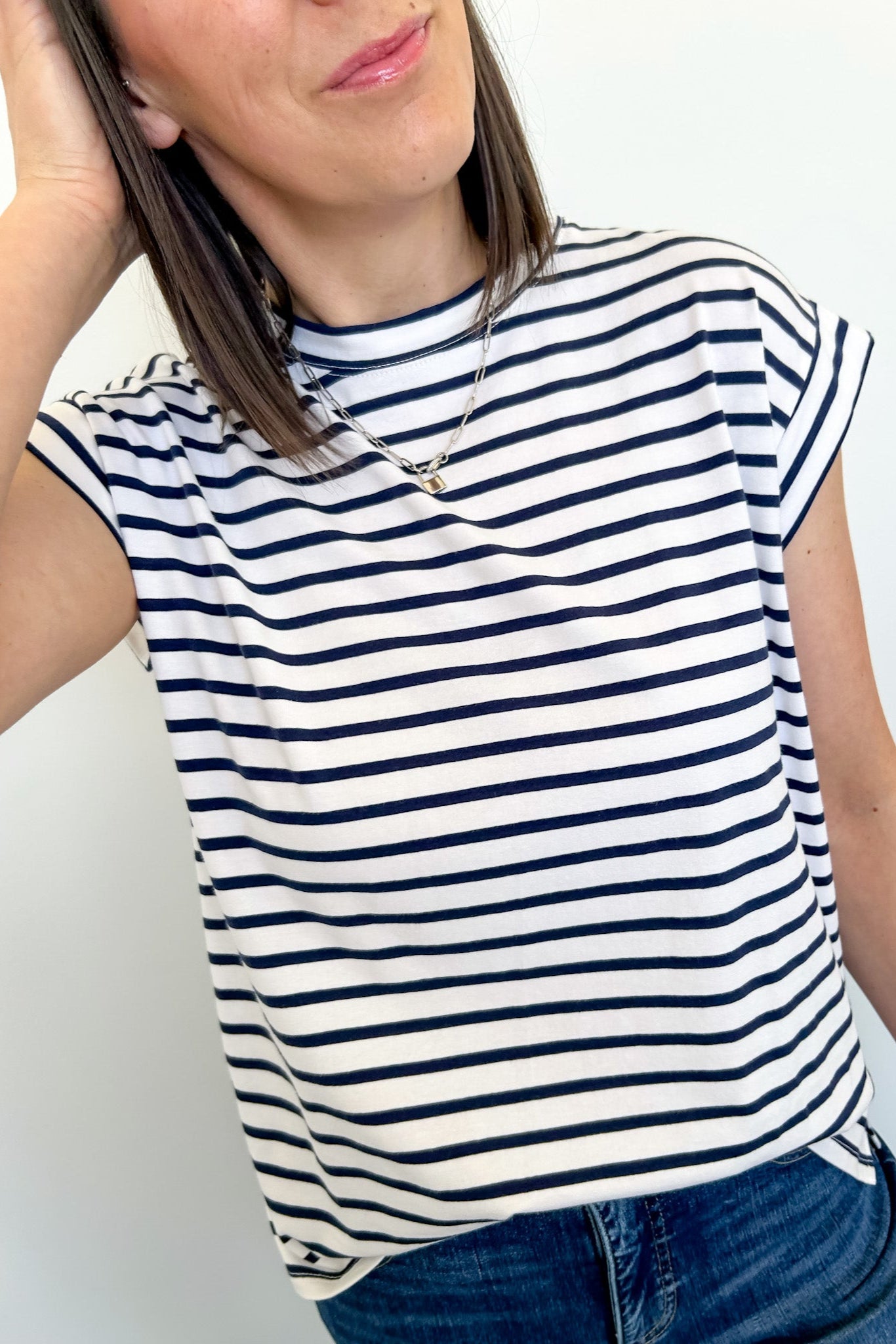 Person wearing a navy and white striped sleeveless top with blue jeans against a plain background