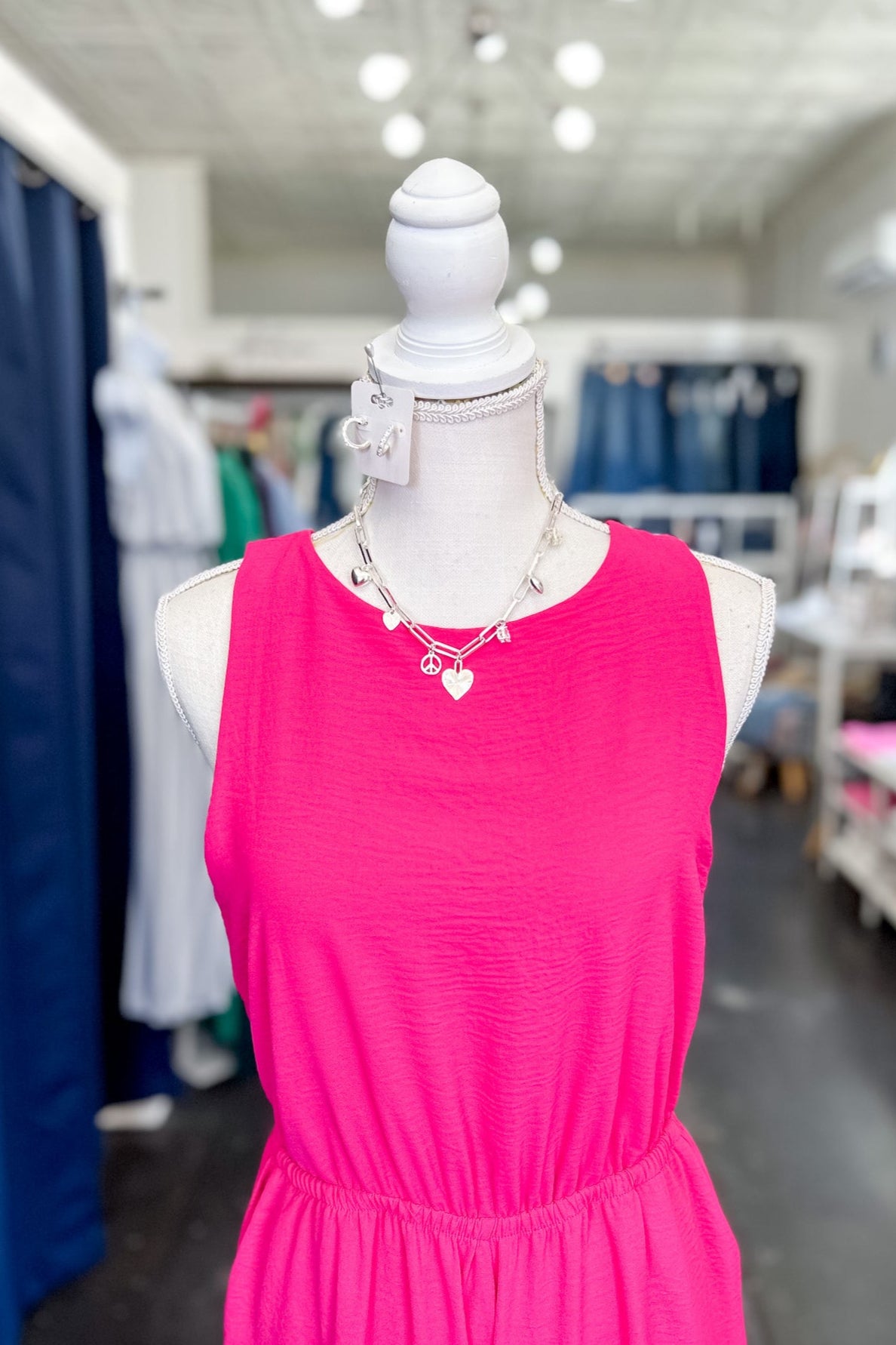 Mannequin wearing a pink dress in a store setting with blue curtains and white ceiling.