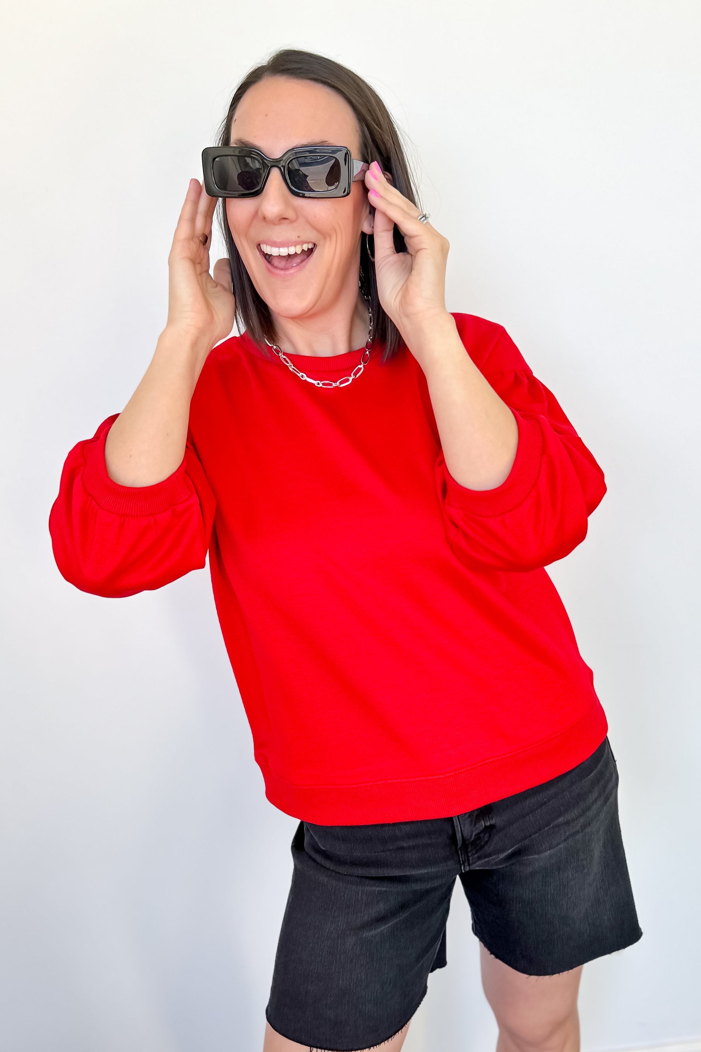 Person wearing a red sweatshirt and black shorts with sunglasses on a white background