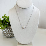 Necklace on a white bust with a plant in the background