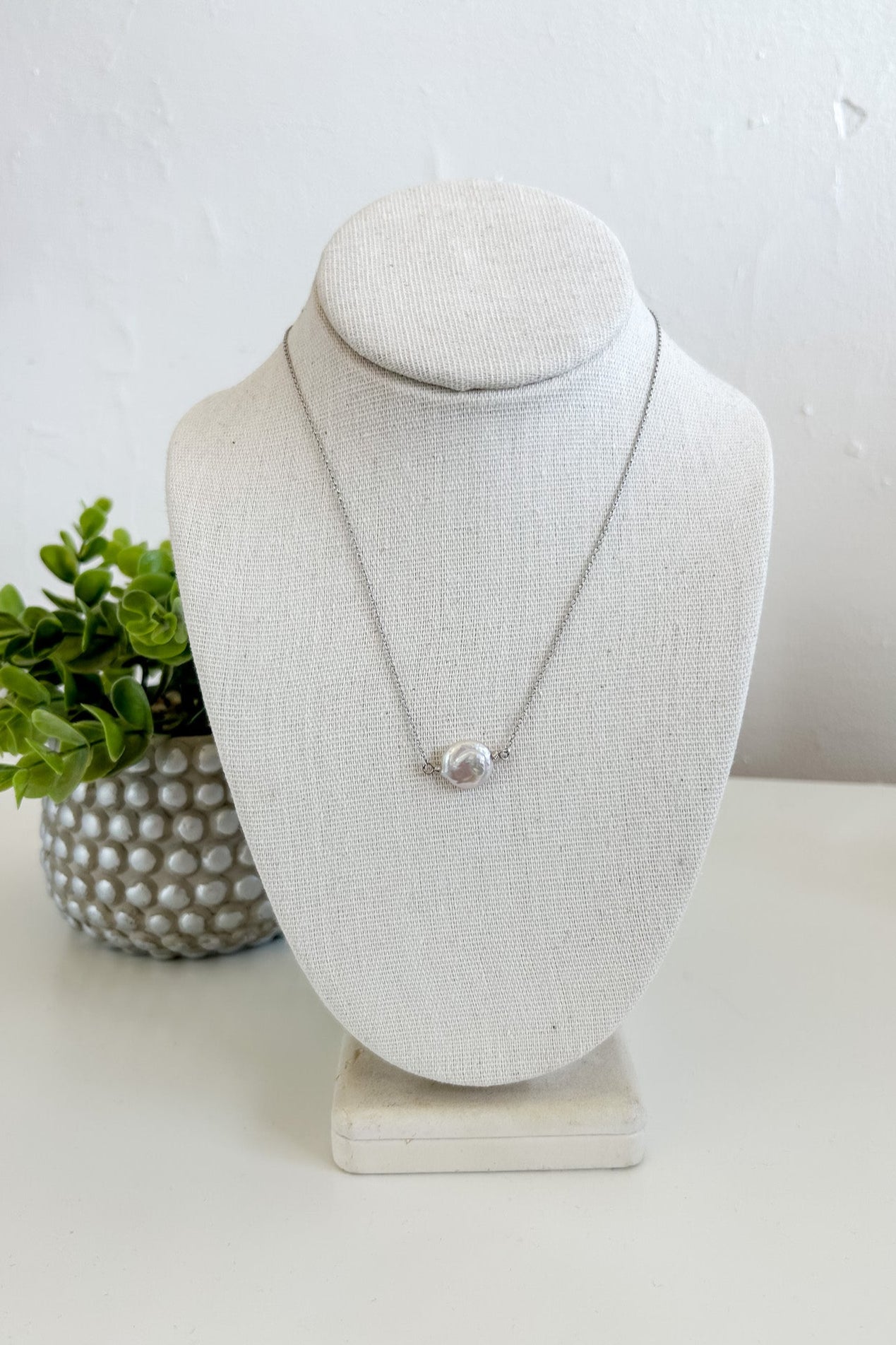 Necklace on a white bust with a plant in the background