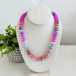 Necklace with multicolored beads on a white stand with a plant in the background