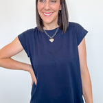 Woman wearing a navy blue cap sleeve top and jeans against a white background