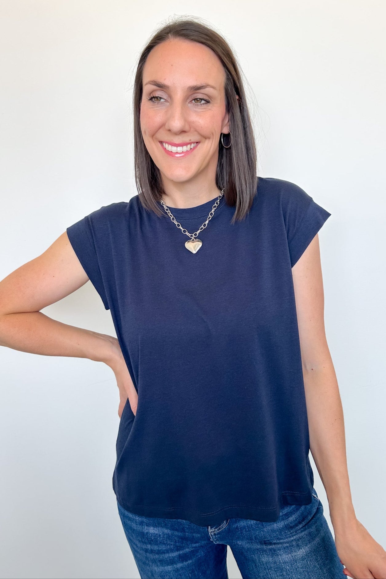 Woman wearing a navy blue cap sleeve top and jeans against a white background