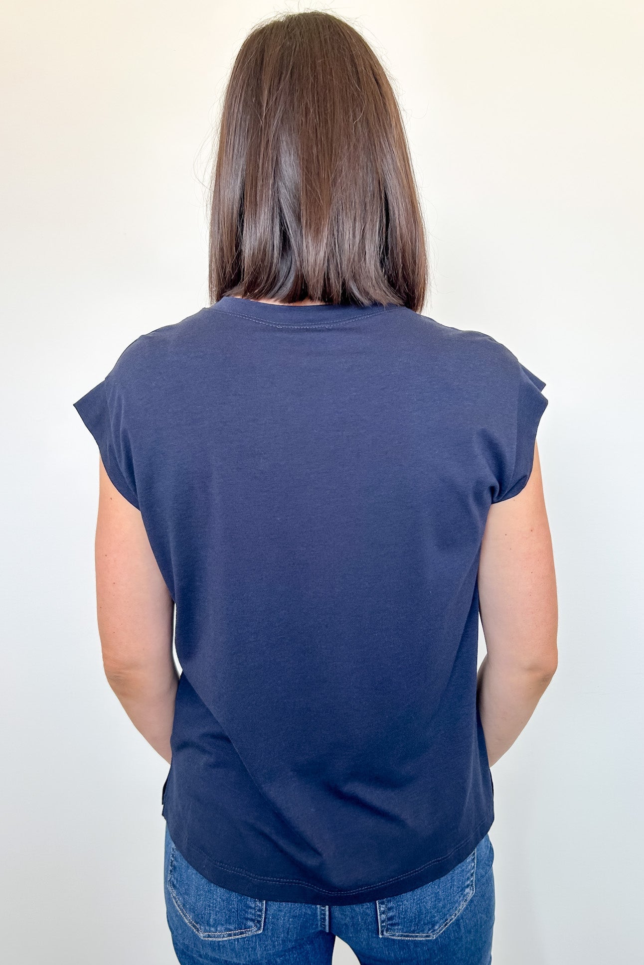 Person wearing a navy blue sleeveless top and jeans against a white background