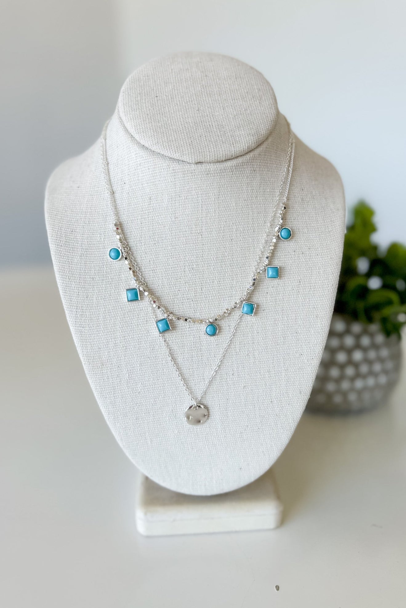 Necklace with turquoise beads on a white bust against a white background