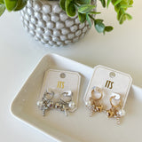 Pair of earrings on cards with a decorative plant in the background