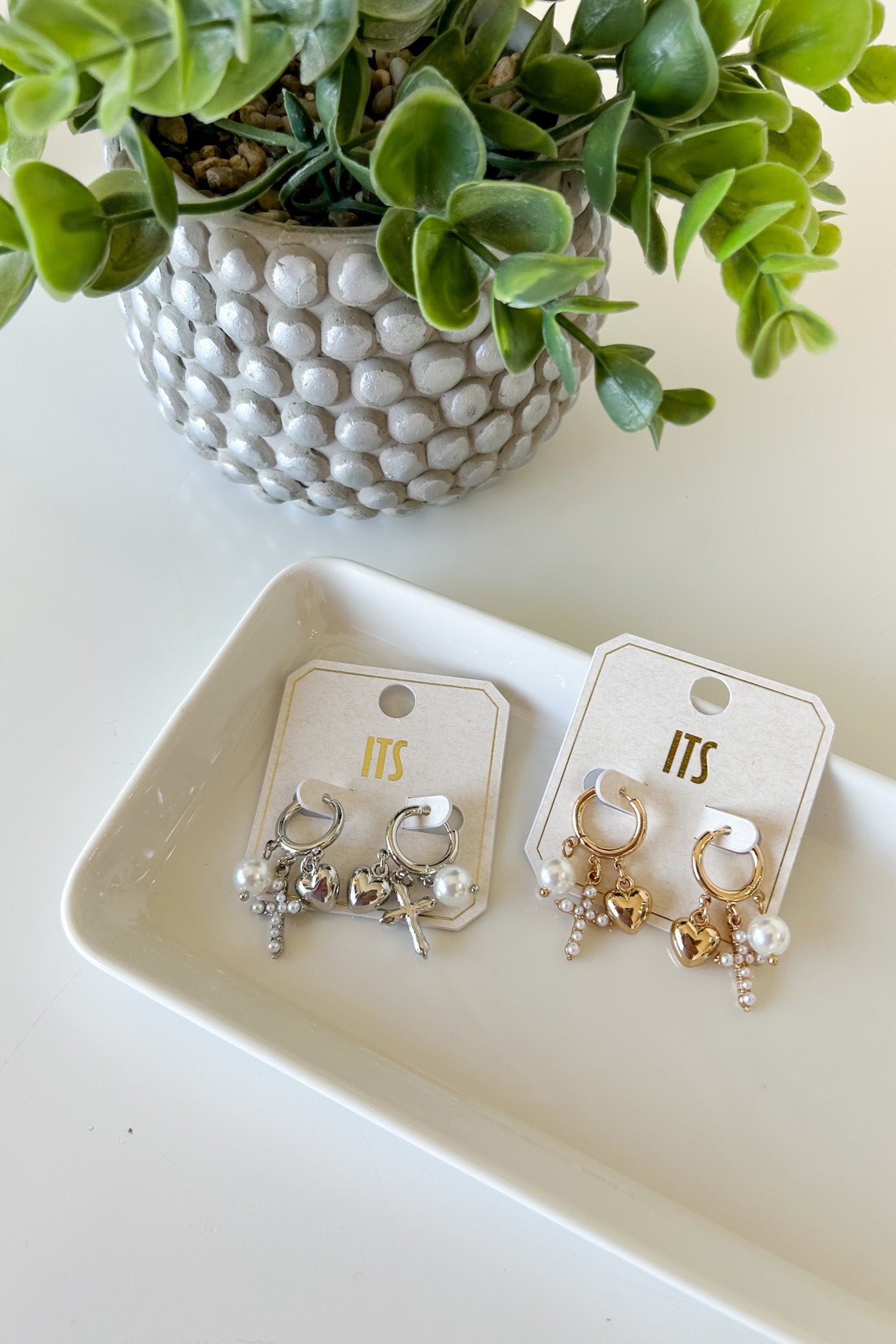 Pair of earrings on cards with a decorative plant in the background