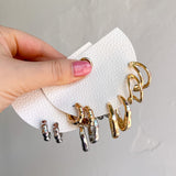 Hand holding a set of gold and silver earrings on a white napkin against a light gray background