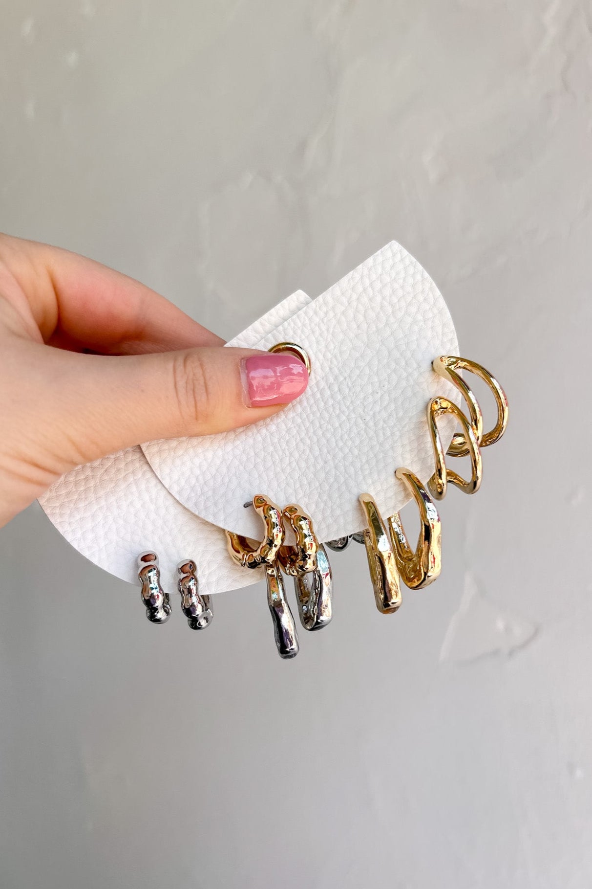 Hand holding a set of gold and silver earrings on a white napkin against a light gray background