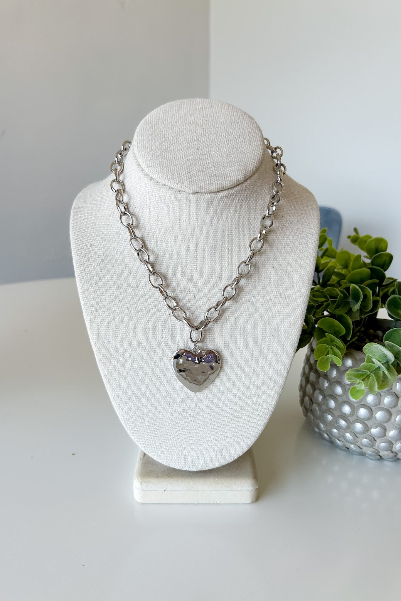 Necklace with a heart pendant on a mannequin bust with a plant in the background