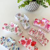 Set of floral-patterned hair claw clips on a light surface with a plant in the background