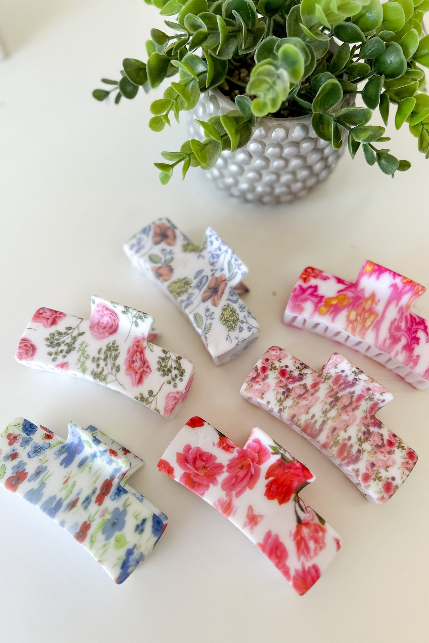 Set of floral-patterned hair claw clips on a light surface with a plant in the background