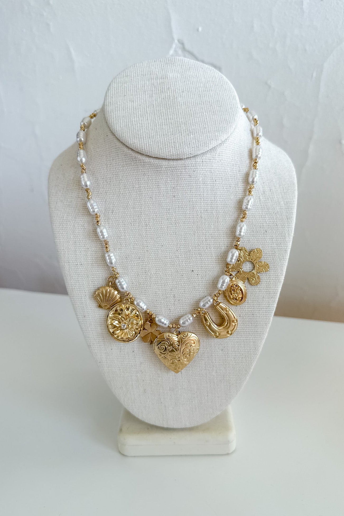 Gold necklace with heart and floral designs on a white bust