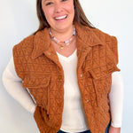 Woman wearing a brown quilted vest over a white shirt and blue jeans against a light background