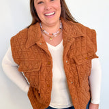 Woman wearing a brown quilted vest over a white shirt and blue jeans against a light background