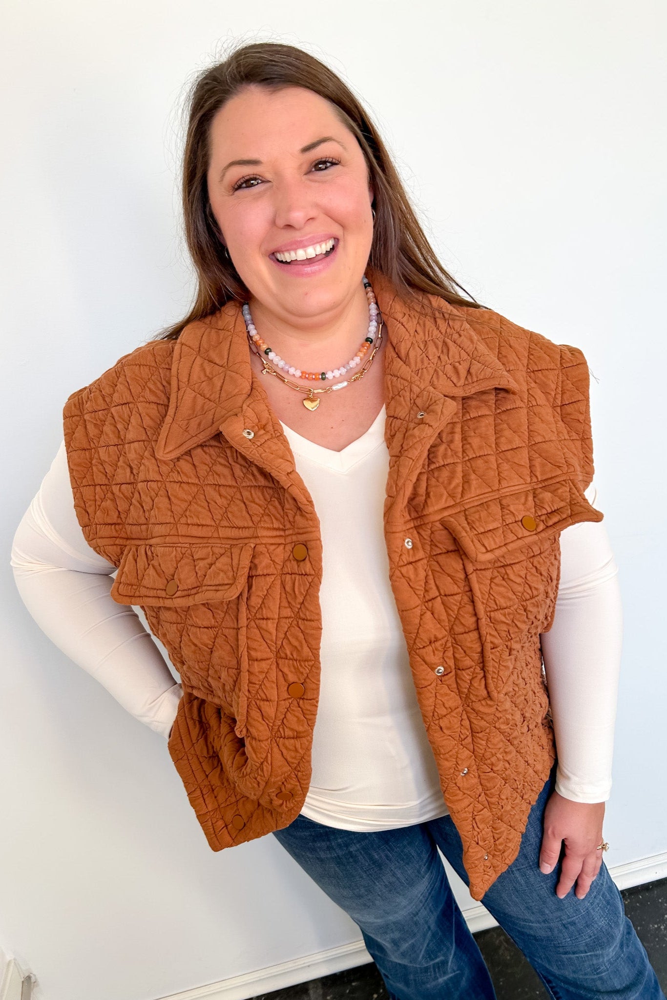 Woman wearing a brown quilted vest over a white shirt and blue jeans against a light background