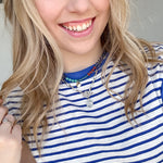 Woman wearing blue and white striped top with necklaces.