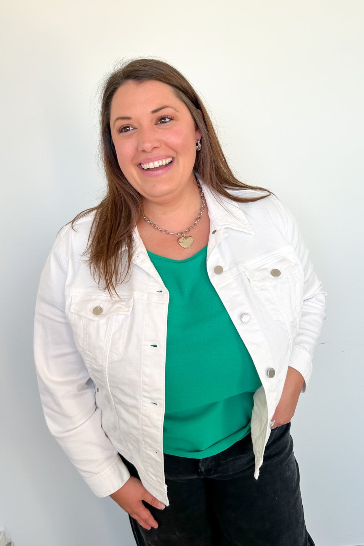 Woman wearing a white jacket over a green top with a plain background
