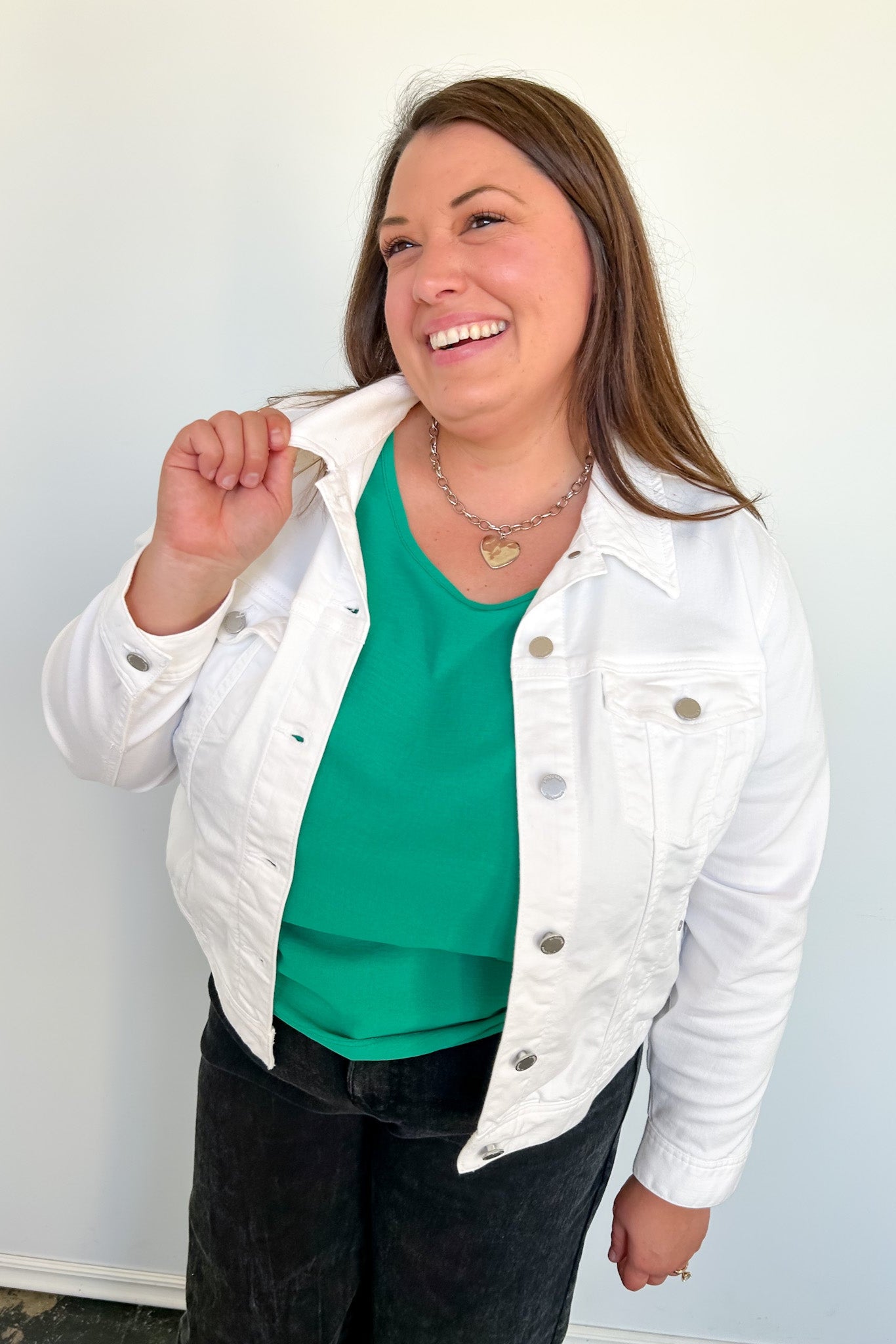 Woman wearing a white denim jacket over a green top against a plain background